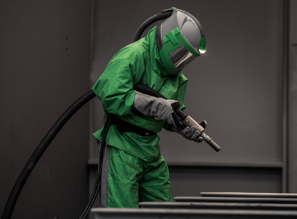 Operatore durante un’attività di sabbiatura con casco Nova 3 e tuta protettiva verde.